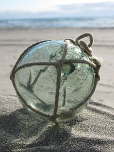 a glass ball sitting on top of sand next to the ocean with a rope wrapped around it