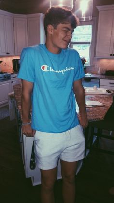 a young man standing in front of a kitchen counter wearing white shorts and a blue champion t - shirt