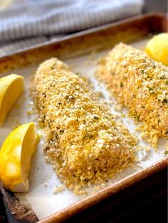 two pieces of breaded fish on a baking sheet with lemons and parmesan cheese