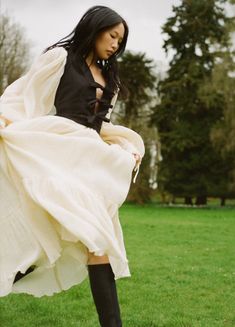 a woman in a white dress and black boots standing on the grass with her legs spread out