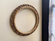 a gold circular mirror hanging on the wall next to a window with curtains behind it