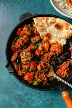 a skillet filled with meat and vegetables on top of a blue table next to rice