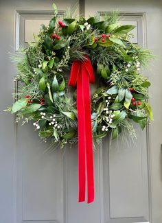 a christmas wreath with red ribbon hanging on the front door and green leaves around it