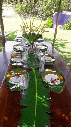 a long wooden table with plates and glasses on it, set for an outdoor meal