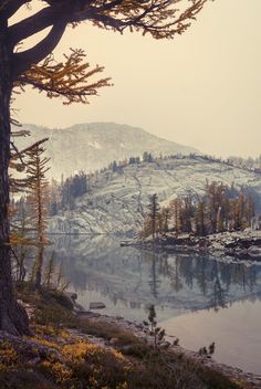 a lake surrounded by mountains and trees with snow on the ground in the foreground