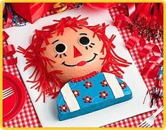 a red haired doll sitting on top of a table next to a blue and white cake