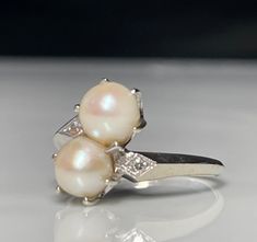 two pearls are sitting on top of a silver ring with white diamonds in the middle