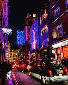 cars are parked on the street in front of tall buildings with neon signs above them