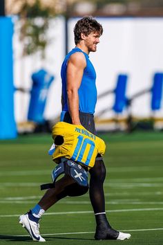 a man in blue shirt and yellow gloves running on field with football equipment behind him