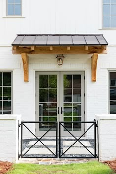 a white brick building with two doors and a black iron fence on the front porch