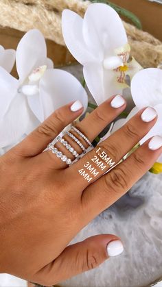 a woman's hand with three rings on it and some flowers in the background