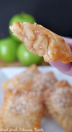 a person holding up a piece of food on top of a white plate with green apples in the background