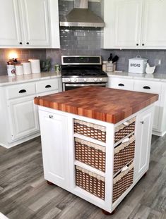 a kitchen island with baskets on it in front of an oven and stove top, surrounded by white cabinets