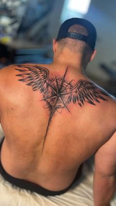 a man with a cross and wings tattoo on his back is looking at the camera