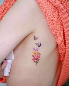 a woman's breast with flowers and butterflies tattooed on her left side ribcage