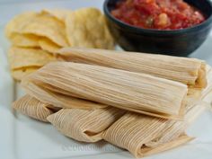 several tamales on a plate with salsa and tortilla chips next to it