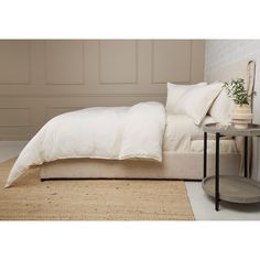 a bed with white linens and pillows in a neutral room next to a side table