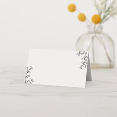 an empty card sitting on top of a table next to a vase with flowers