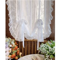 the curtains are hanging in front of the table with flowers and other items on it