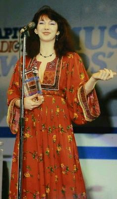 a woman standing in front of a microphone holding a book and wearing a red dress