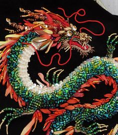 a close up of a dragon made out of beads on a black cloth with red string