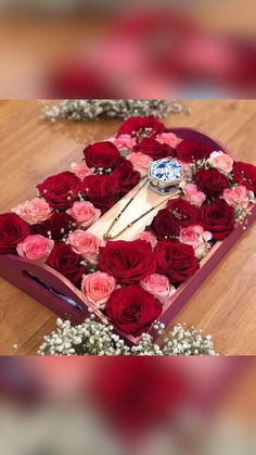 a heart shaped box filled with roses on top of a wooden floor next to a necklace