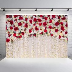 a white brick wall with red and white flowers hanging on it's side in front of a backdrop