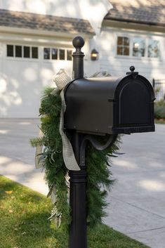 a mailbox decorated with greenery and ribbon in front of a house on a sunny day