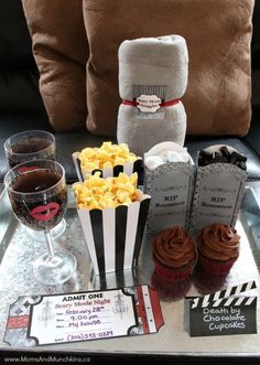 a tray topped with cupcakes and popcorn next to two glasses of red wine