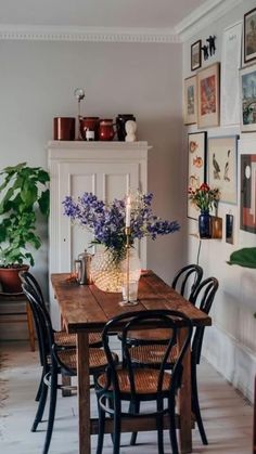 a wooden table topped with lots of chairs next to a vase filled with purple flowers