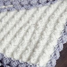 a crocheted blanket is laying on top of a wooden table and it's blue and white colors