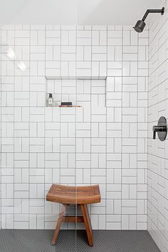 a white tiled bathroom with a wooden bench in the corner and shower head mounted to the wall