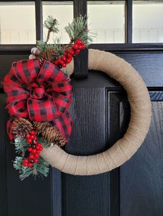 a christmas wreath with pine cones and red berries hanging on a black front door handle