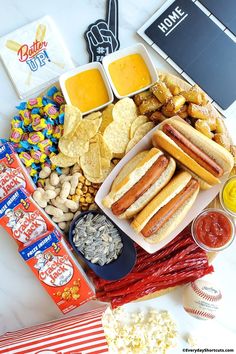 hot dogs, chips, and condiments are arranged on a table with snacks