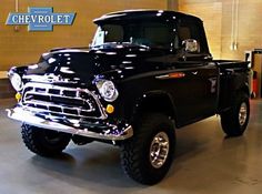 an old black pickup truck parked in a garage next to a sign that says chevrolet