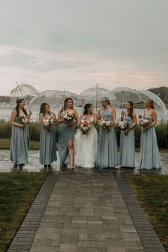 a group of women standing next to each other on top of a brick walkway holding umbrellas