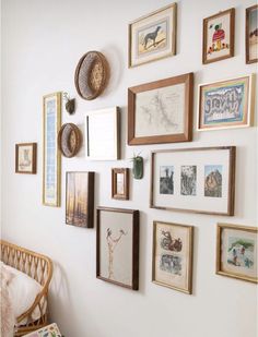 a wall with many framed pictures on it and a wicker chair in the corner