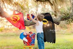 a young boy holding onto a bat and superman cape in front of a tree branch