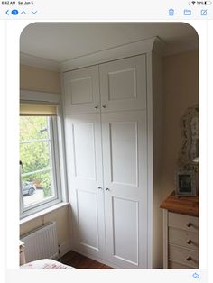 an image of a bedroom setting with white cupboards and drawers on the wall next to a window