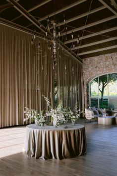 a table with flowers on it in front of a curtained wall and chairs around it