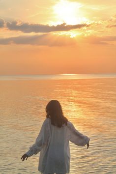 a woman standing in the water with her arms spread out to the side at sunset