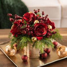 a vase filled with red flowers on top of a wooden table next to gold ornaments