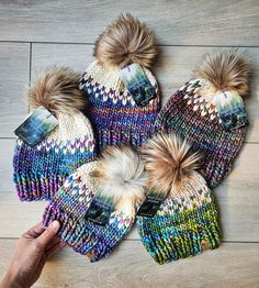 four hats and two mittens are on the floor with one person's hand