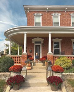 a large brick house with white columns and red flowers on the front steps, surrounded by greenery