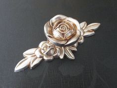 a silver rose brooch sitting on top of a black table next to a pair of scissors