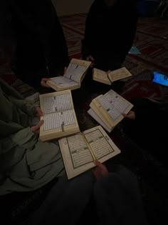 four people sitting on the floor holding open books in their hands, with one person looking at them