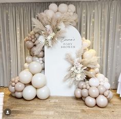 a white sign surrounded by balloons in front of a curtained backdrop with flowers and feathers