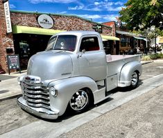 an old silver truck parked in front of a building on the side of the road