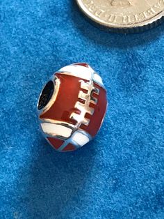 a red and white football bead sitting on top of a blue surface next to a penny