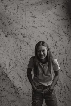 a girl standing in front of a wall with her hands on her hips and smiling